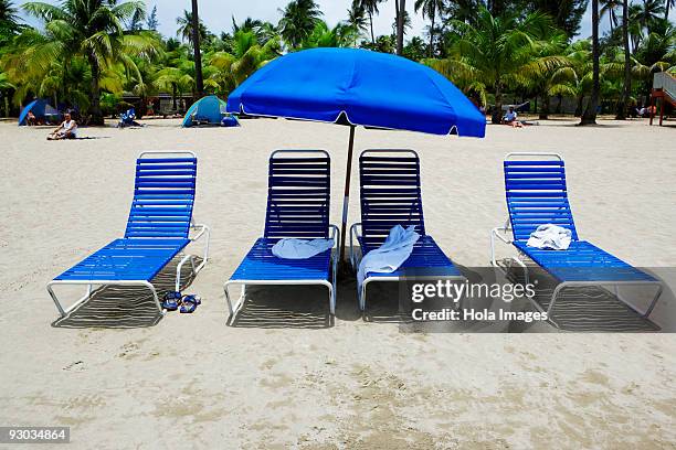 lounge chairs under a beach umbrella on the beach, luquillo beach, puerto rico - luquillo stock-fotos und bilder