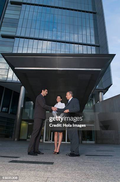 two businessmen shaking hands in front of an office building - low angle view of two businessmen standing face to face outdoors stock pictures, royalty-free photos & images