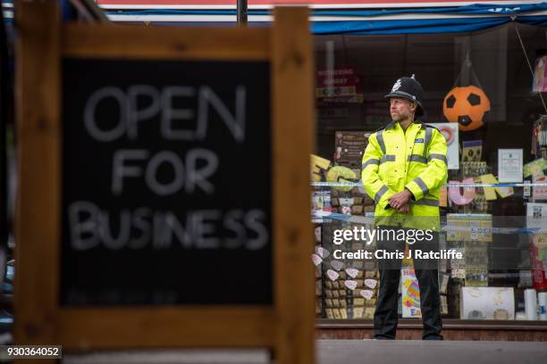 Sign showing that local shops are open for business stands near a police officer at a cordon near to the bench where investigations continue into the...