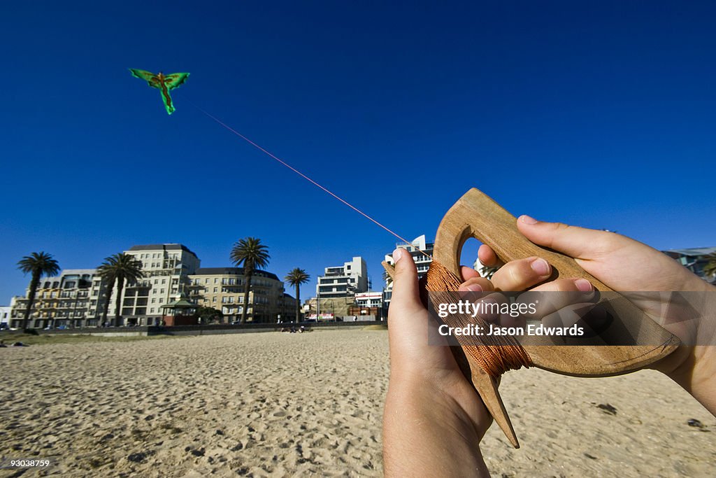 The hands of a young boy flying a bright green Balinese dragon kite.