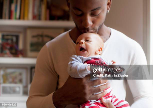 father holding and kissing his newborn baby - bebe metisse photos et images de collection