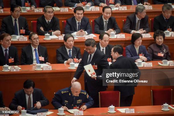 Chinese President Xi Jinping hands over a folder as he leaves during the third plenary session of the first session of the 13th National People's...