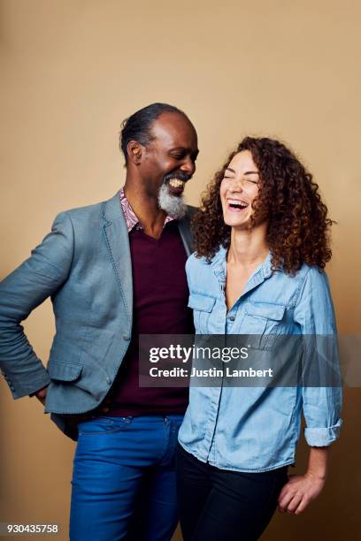 older man and a younger woman laughing and sharing a moment together on a neutral backdrop - older woman younger man stock-fotos und bilder