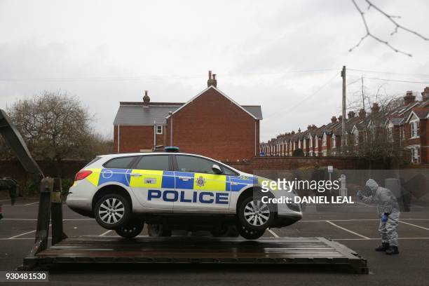Military personnel wearing protective coveralls use a fork-lift to load a police car onto a military vehicle for it to be taken away from a cordoned...