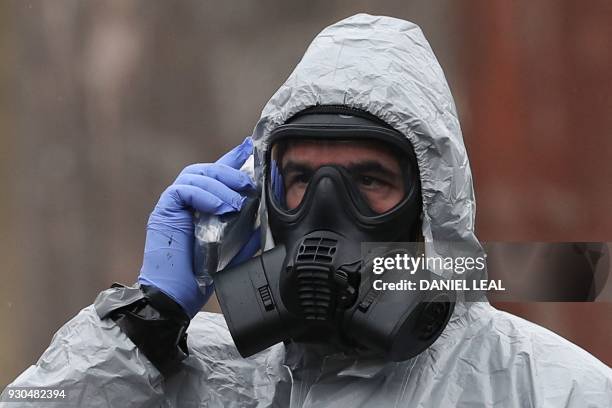 Military personnel speaks on a device wearing protective coveralls as he works to remove vehicles from a cordoned off area behind a police station in...