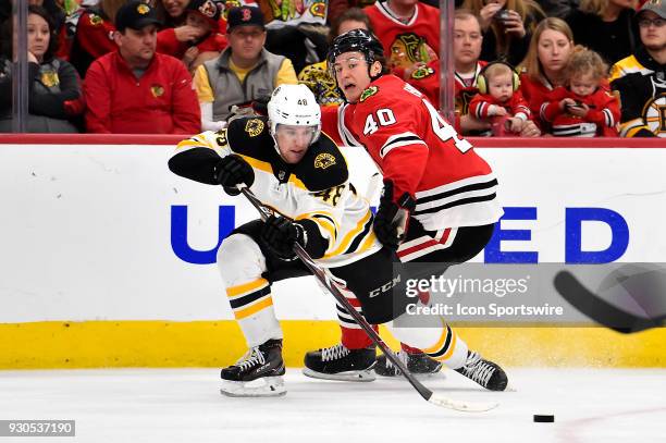 Boston Bruins defenseman Matt Grzelcyk and Chicago Blackhawks right wing John Hayden battle for the puck during the second period on March 11, 2018...