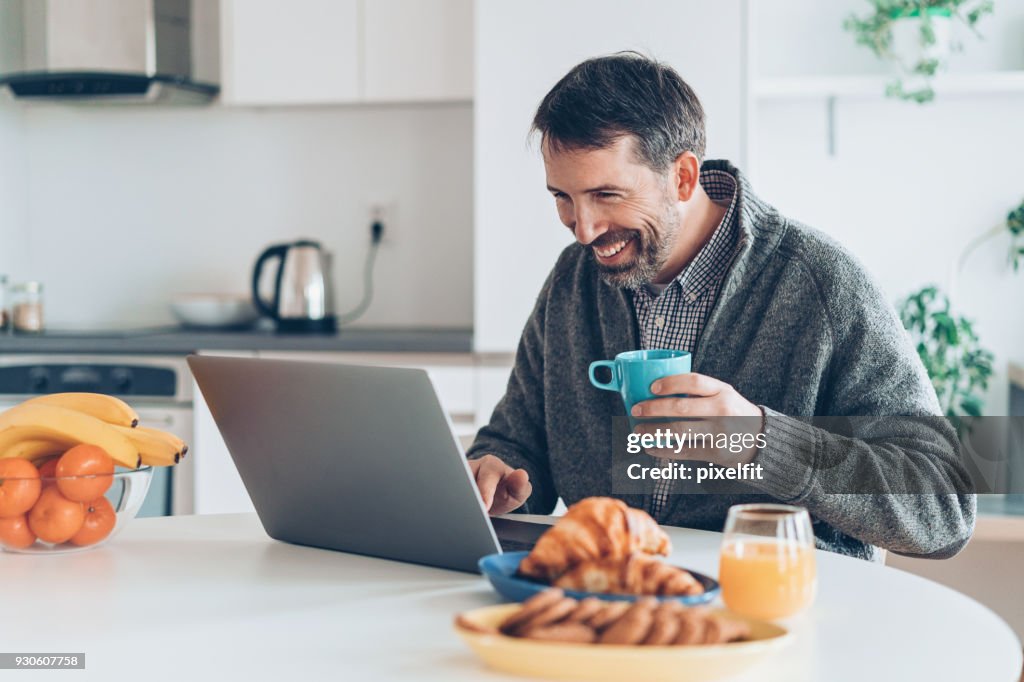 Homme avec ordinateur portable dans la cuisine d’âge moyen