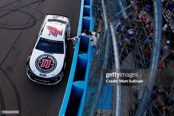 Kevin Harvick, driver of the Jimmy John's Ford, takes the checkered flag from the NASCAR official after winning the Monster Energy NASCAR Cup Series...