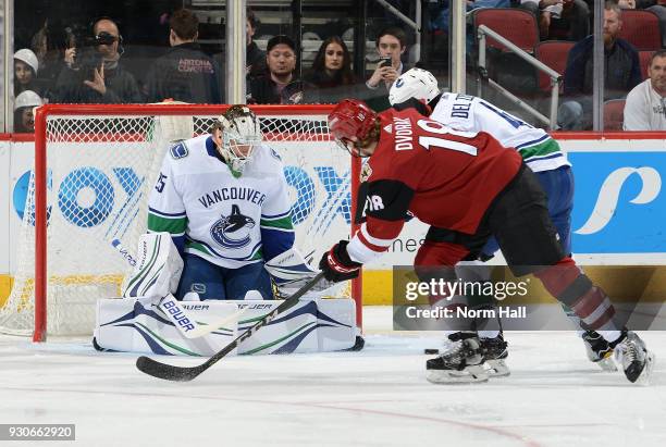 Goalie Jacob Markstrom of the Vancouver Canucks deflects the puck away from the net on the shot by Christian Dvorak of the Arizona Coyotes as Michael...