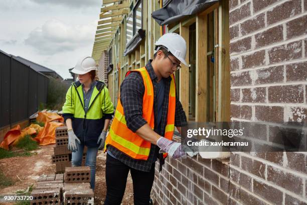 female worker assisting bricklayer at site - bricklayer stock pictures, royalty-free photos & images