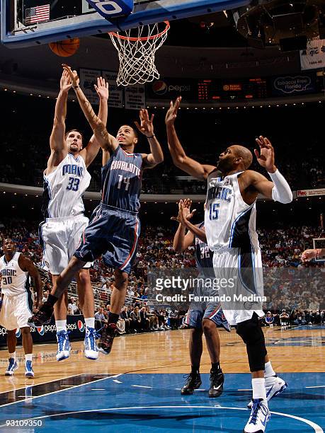 Augustin of the Charlotte Bobcats takes the ball to the basket between Ryan Anderson and Vince Carter of the Orlando Magic during the game on...