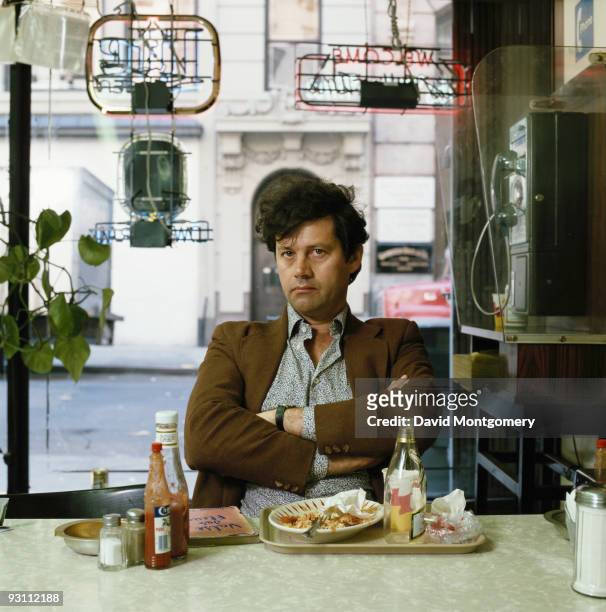 Australian film director Bruce Beresford dines at a cafe, circa 1980. On the table in front of him is a copy of 'Valse des Fleurs' by English poet...
