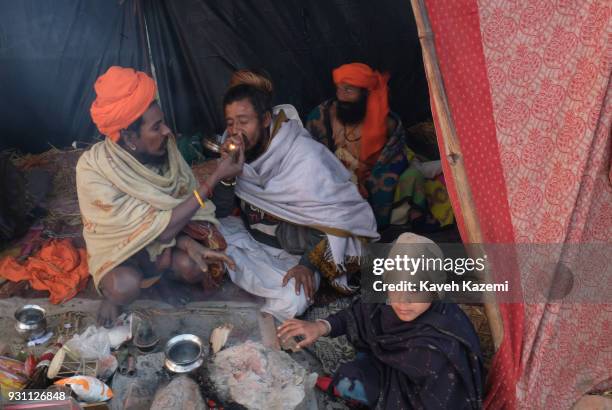 The Indian Hindu Sadhus seen sat in their tent smoking a chillum full of hashish at sunrise near Sangam which is the point of confluence of River...