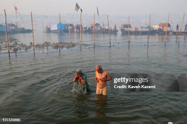 An Indian Hindu devotee old couple seen at sunrise taking a holy dip in Sangam which is the point of confluence of River Ganga, Yamuna and...