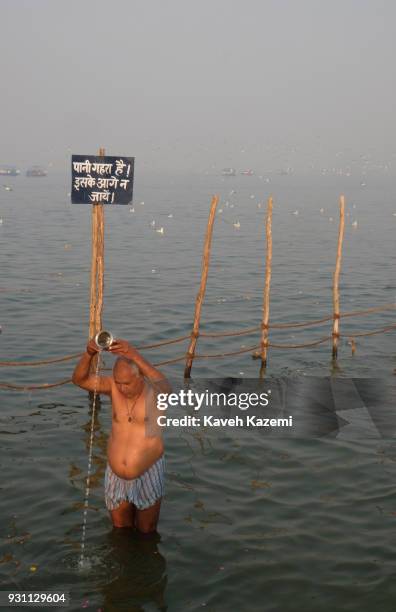 An Indian Hindu devotee man performs a religious ceremony by pouring water out of a steel can while bathing in Sangam which is the point of...