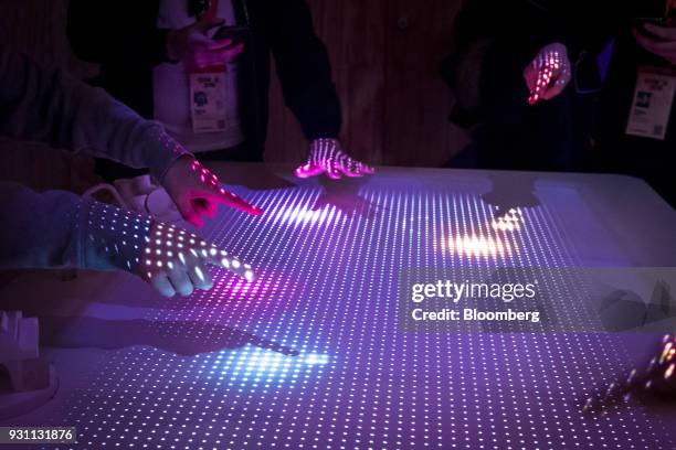 Attendees point to light patterns on a table being lit by the Interactive Tabletop Projector inside the Sony Corp. Wow Studio during the South By...
