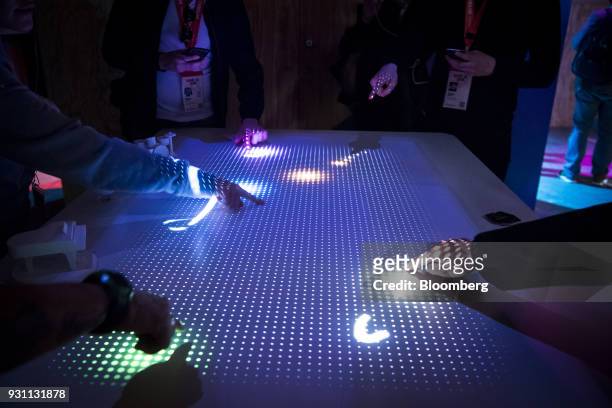 Attendees point to light patterns on a table being lit by the Interactive Tabletop Projector inside the Sony Corp. Wow Studio during the South By...