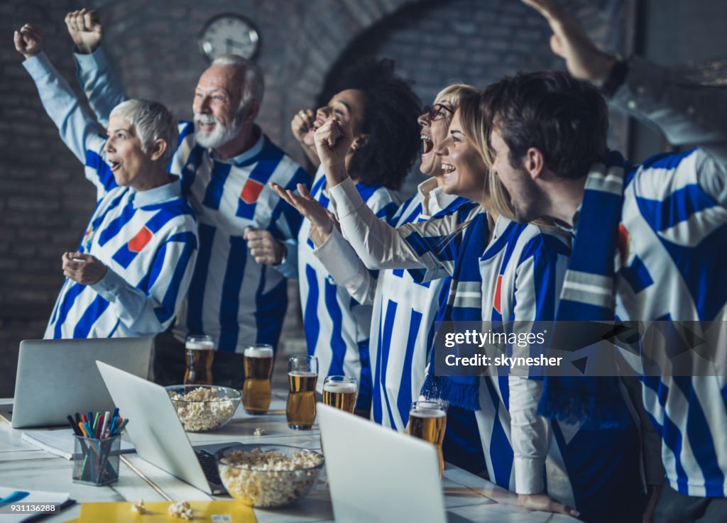 Grupo grande de gente de negocios feliz animando a su equipo de fútbol mientras mira TV en la oficina.