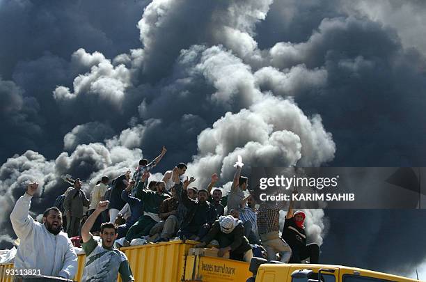 Iraqis sitting on a truck loaded with medical and food supplies bound for the flashpoint town of Fallujah, celebrate while passing a burning US...
