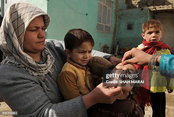An Afghan woman holds a child as a health worker administers polio vaccine on the second day of a vaccination campaign in Kabul on November 16, 2009....