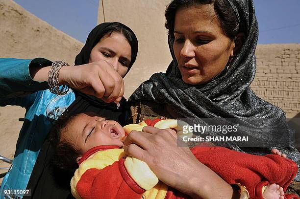An Afghan woman holds a child as a health worker administers polio vaccine on the second day of a vaccination campaign in Kabul on November 16, 2009....