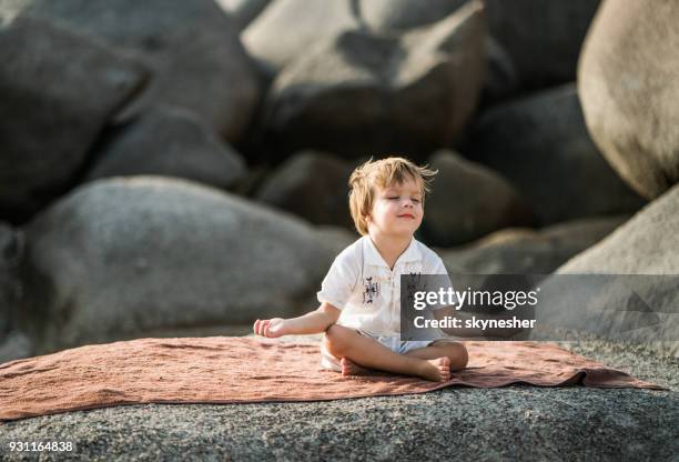 little boy sitting on a rock at the beach and doing meditation exercises in lotus position. - the silent boy stock pictures, royalty-free photos & images
