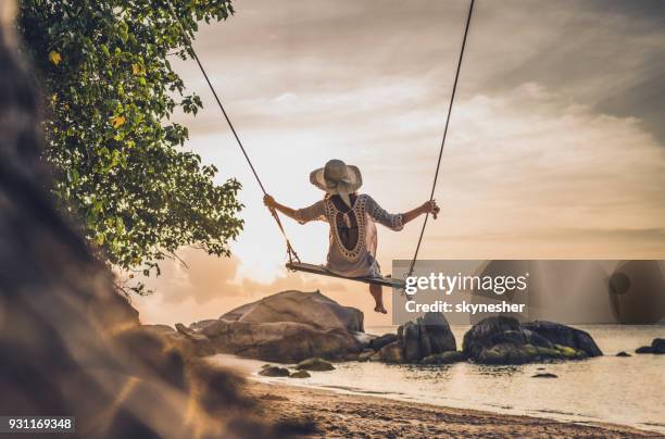 rear view of a woman swinging during summer vacation on a beach. - swinging stock pictures, royalty-free photos & images