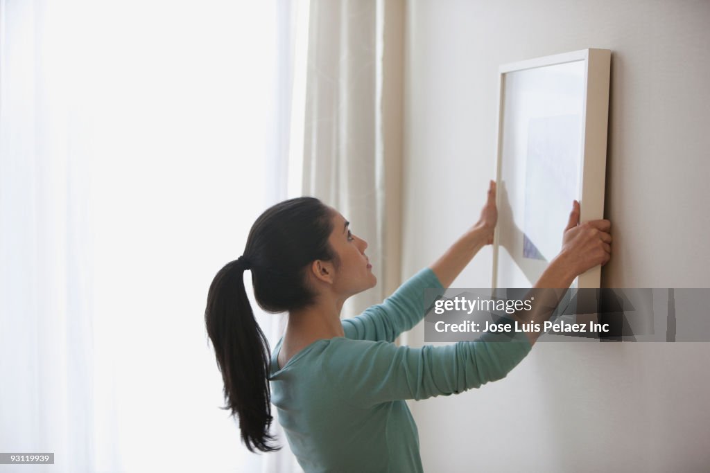 Mixed race woman hanging picture on wall