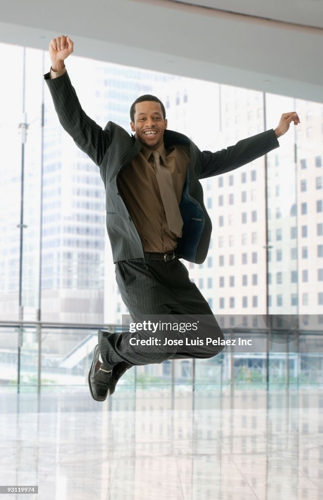 Mixed race businessman jumping in office