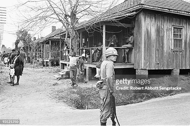 An MP leans on his rifle as the stands on a streetcorner, while men and women sit on porches and stand on the sidewalk during on the Selma to...