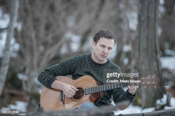 musician man in a snowy forest with his guitar and sitting on a tree branch - musical instrument string stock pictures, royalty-free photos & images