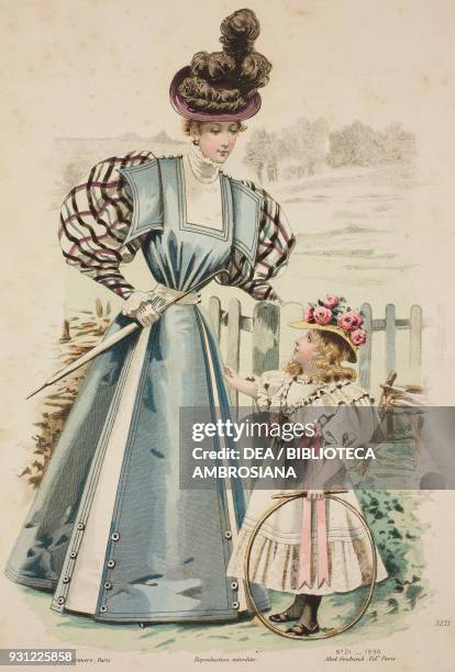 Woman wearing a blue walking dress with checked-puffed sleeves, and carrying an umbrella, girl wearing a pink and white walking dress and hat with...