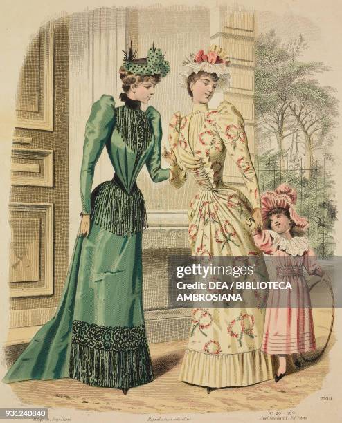 Women wearing decorative green and beige walking dresses and matching hats, little girl wearing a pink walking dress and hat, holding a hoop rolling,...