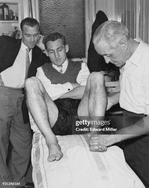 Trainer Frank Penn works on Fulham footballer Roy Bentley's injured ankle at Craven Cottage, London, 18th March 1958. Watching them is player Jim...