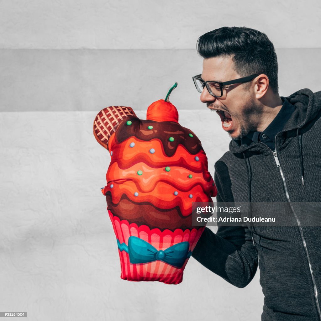 Man Holding Artificial Cupcake Against Wall