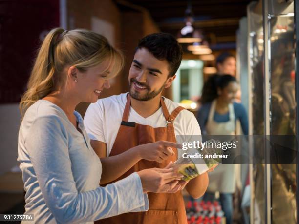 cheerful salesman suggesting a new salad to a beautiful customer both smiling - supermarket staff stock pictures, royalty-free photos & images