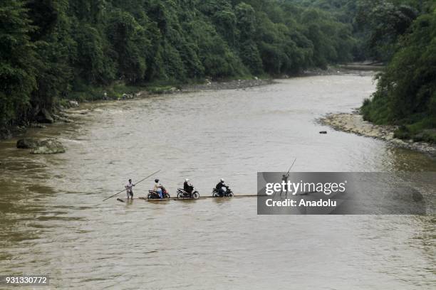 Several people assist motorcyclists to pull up their vehicles onto wooden raft to cross Cisadane River, in Rumpin, Bogor, West Java, Indonesia on...