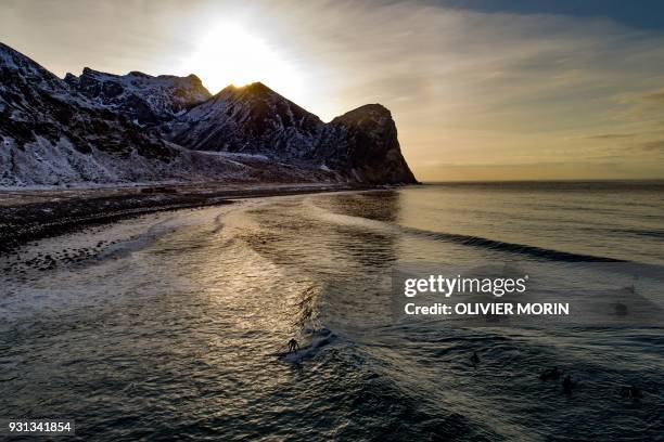 Surfer rides a wave on March 10, 2018 in Unstad, northern Norway, Lofoten islands, within the Arctic Circle as air temperature drops minus 13°C and...