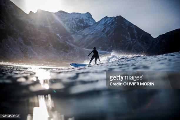 Surfer rides a wave on March 10, 2018 in Unstad, northern Norway, Lofoten islands, within the Arctic Circle as air temperature drops minus 13°C and...