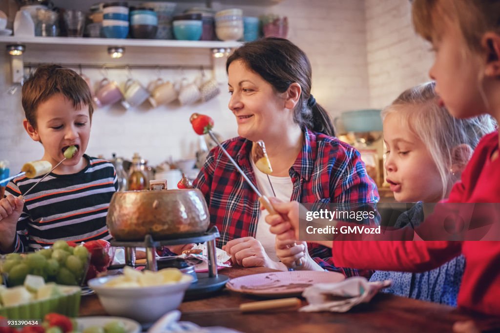 Young Family Having Delicious Chocolate Fondue In A Pot Served With young-family-having-delicious-chocolate-fondue-in-a-pot-served-with