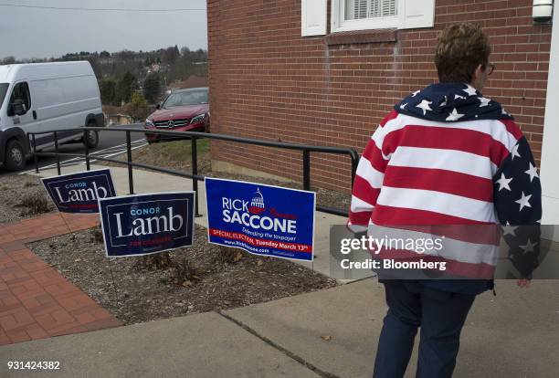 Polling volunteer wearing an American flag sweatshirt walks past campaign signs for Conor Lamb, Democratic candidate for the U.S. House of...