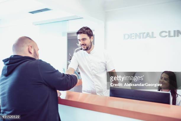 junger zahnarzt und seine assistentin termin an der rezeption in zahnklinik - dentist waiting room stock-fotos und bilder