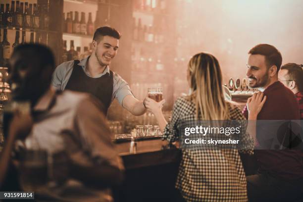 happy bartender serving his customers with beer in a pub. - bartender stock pictures, royalty-free photos & images