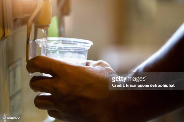 male hand serving water of a water cooler in plastic cup. - cup office stock pictures, royalty-free photos & images