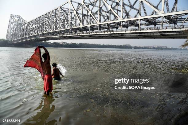 Locals seen taking bath next to the Howrah bridge in Kolkata. The Rabindra Setu also known as the Howrah bridge is a bridge with a suspended span...