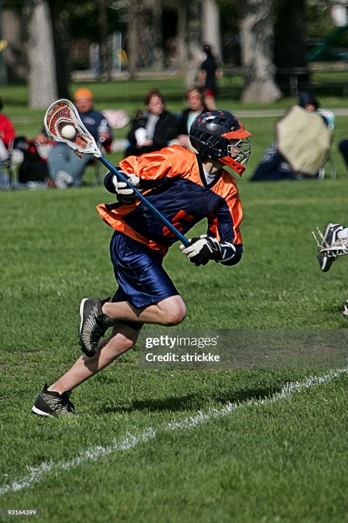 Male Lacrosse Player in Blue Orange Springs to Action Attack