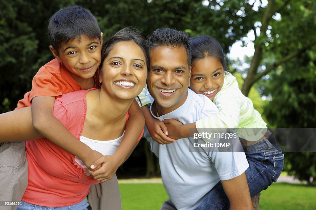 Indian parents giving piggyback ride to their children outdoors