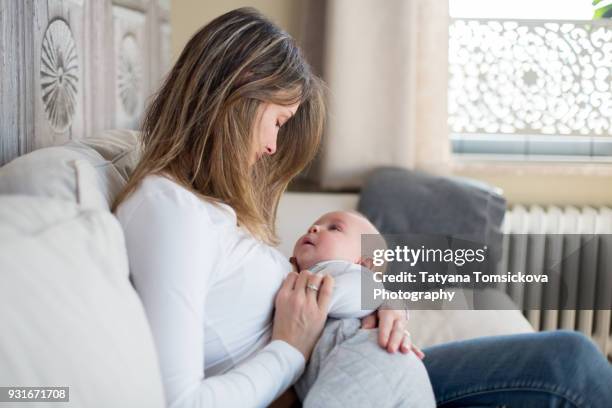 young mother, holding her toddler boy, breastfeeding him at home, sunny living room - toddler milk stock-fotos und bilder