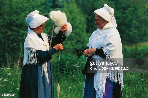 Women wearing hats and shawls, traditional Waldensian costume, spinning wool with a spindle, Piedmont, Italy.