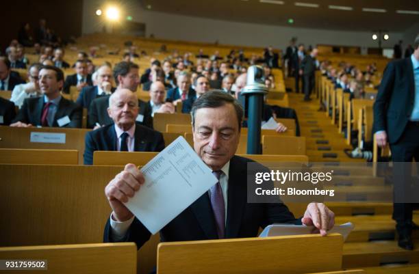 Mario Draghi, president of the European Central Bank , holds a document while sitting in the audience before addressing the 'ECB and its Watchers'...